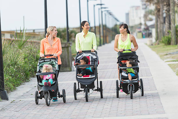 A group of three multi-ethnic mothers walking together, pushing their children in jogging strollers.  The child on the left, a 22 month old toddler with blond hair, is the oldest.  The African American girl and Asian boy are 11 months old.