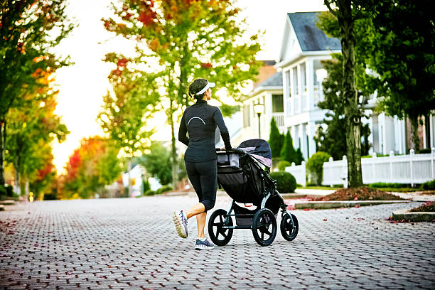 Young woman with baby stroller walking her dog in a neighborhood with houses in the background.